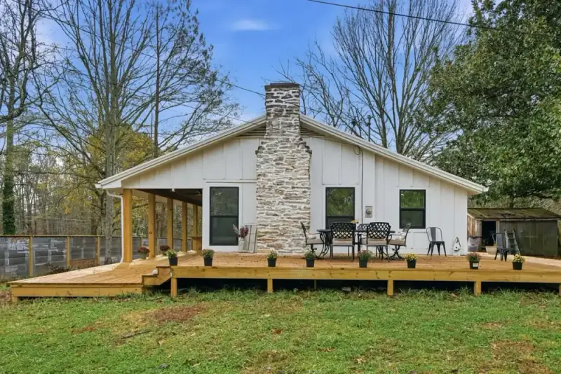 Front view of 356 Hyde Road with a stone chimney, covered porch, lawn, and wooded setting
