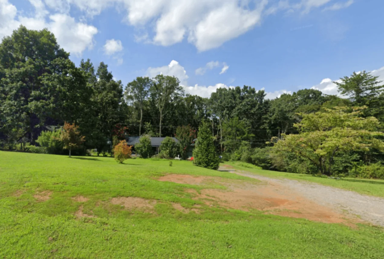 View across the lawn toward the home, trees, and gravel driveway at A-504 Young Loop in Fairmount